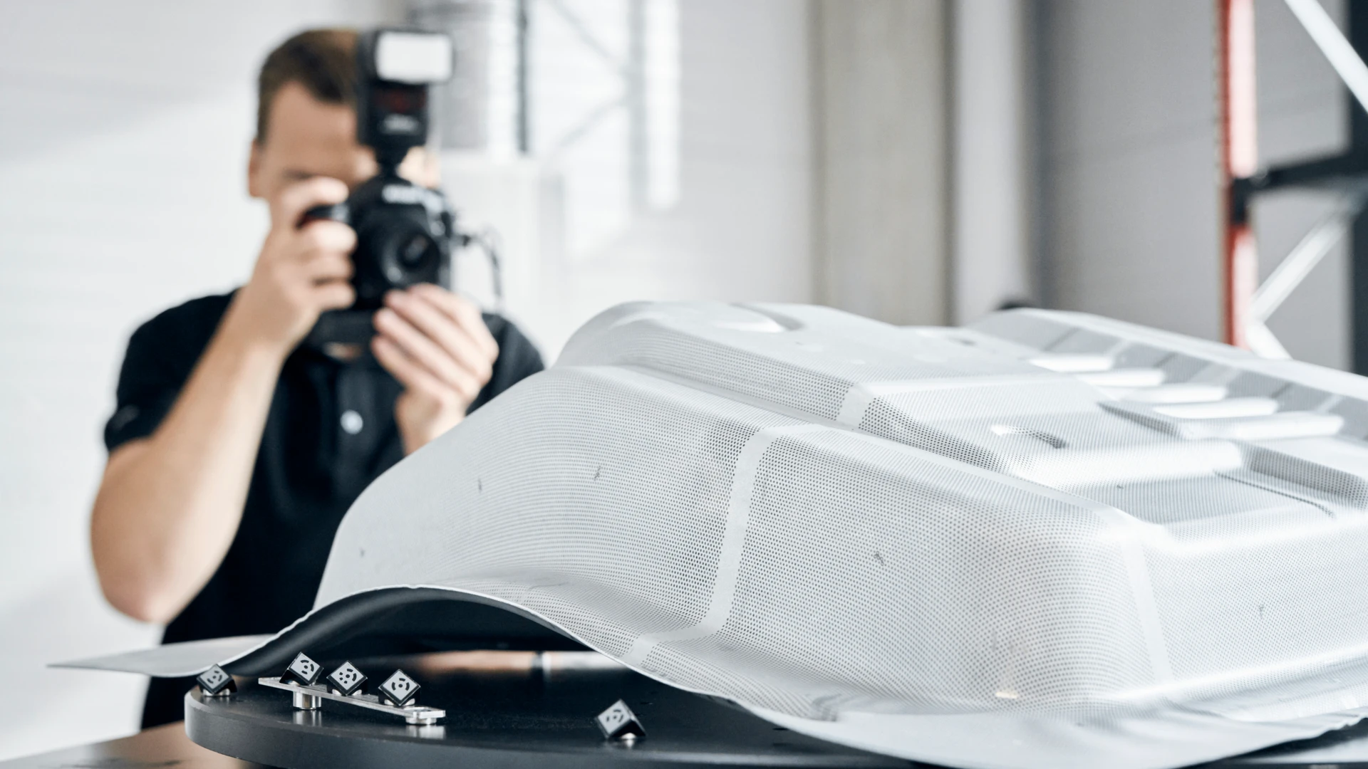 Photographer capturing a formed sheet-metal panel marked with the ARGUS measuring grid, reference crosses laid beside it