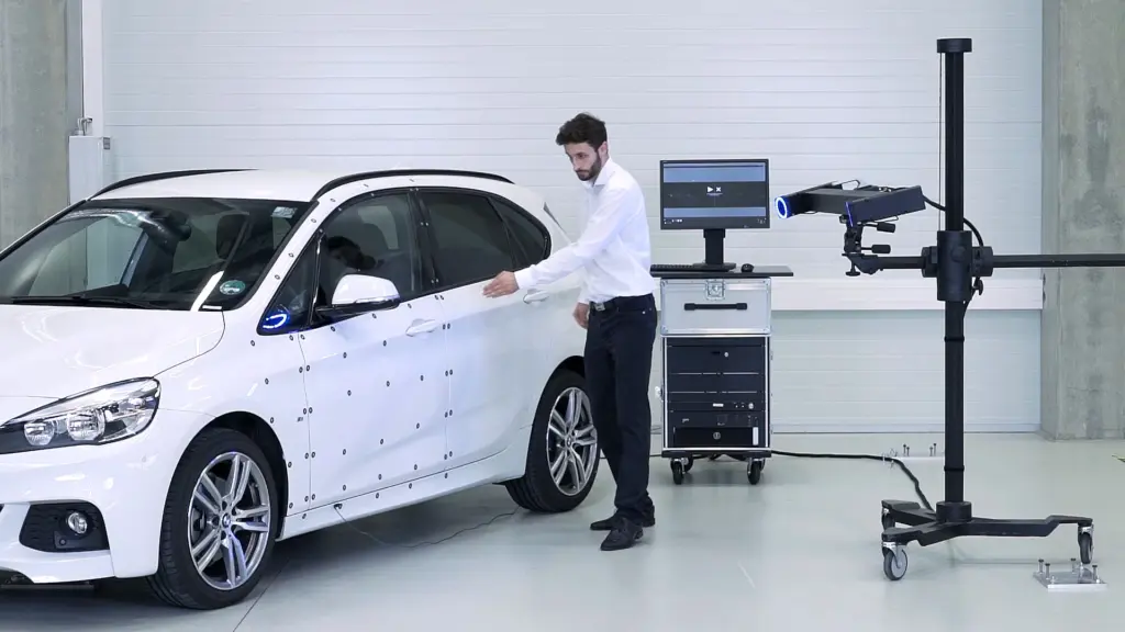 Engineer swinging the door of a white car covered in measuring dots during an ARAMIS door-slam test