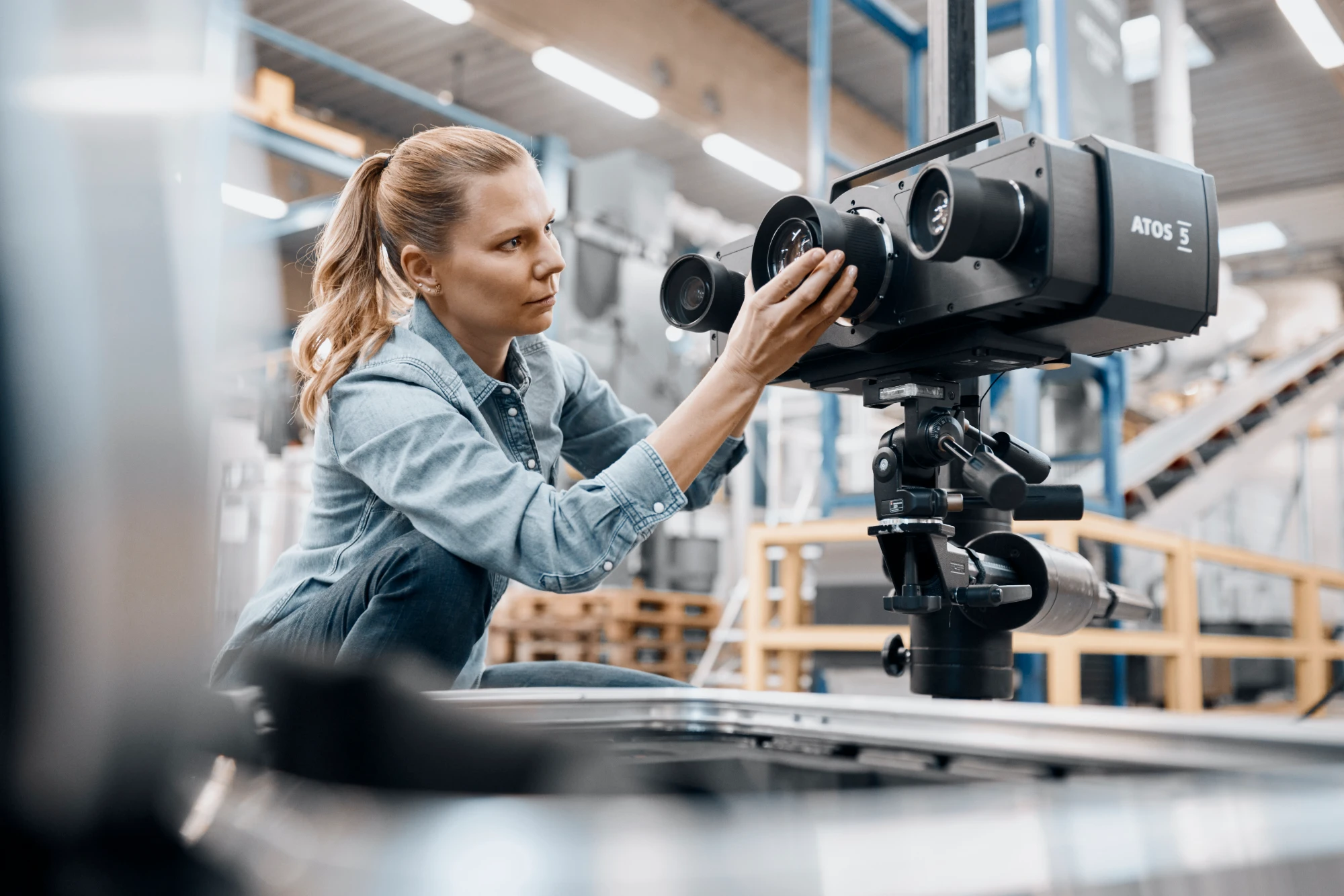 Engineer adjusting the lens of a tripod-mounted ZEISS ATOS 5 scanner in a production hall