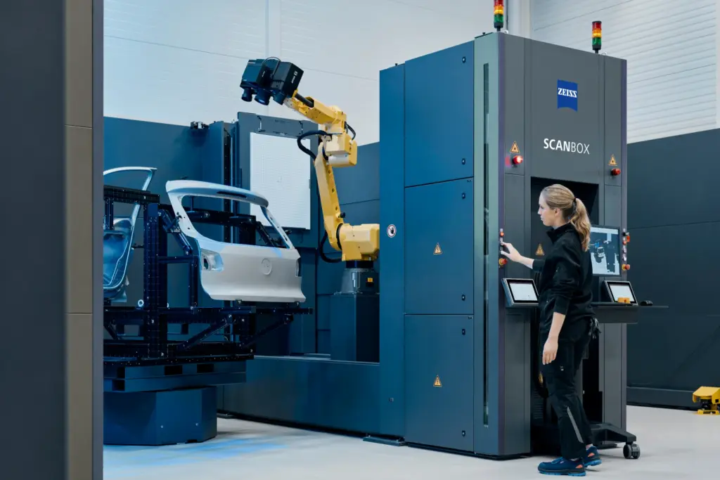ZEISS ScanBox with a yellow robot arm scanning a car door panel while an operator works the control terminal