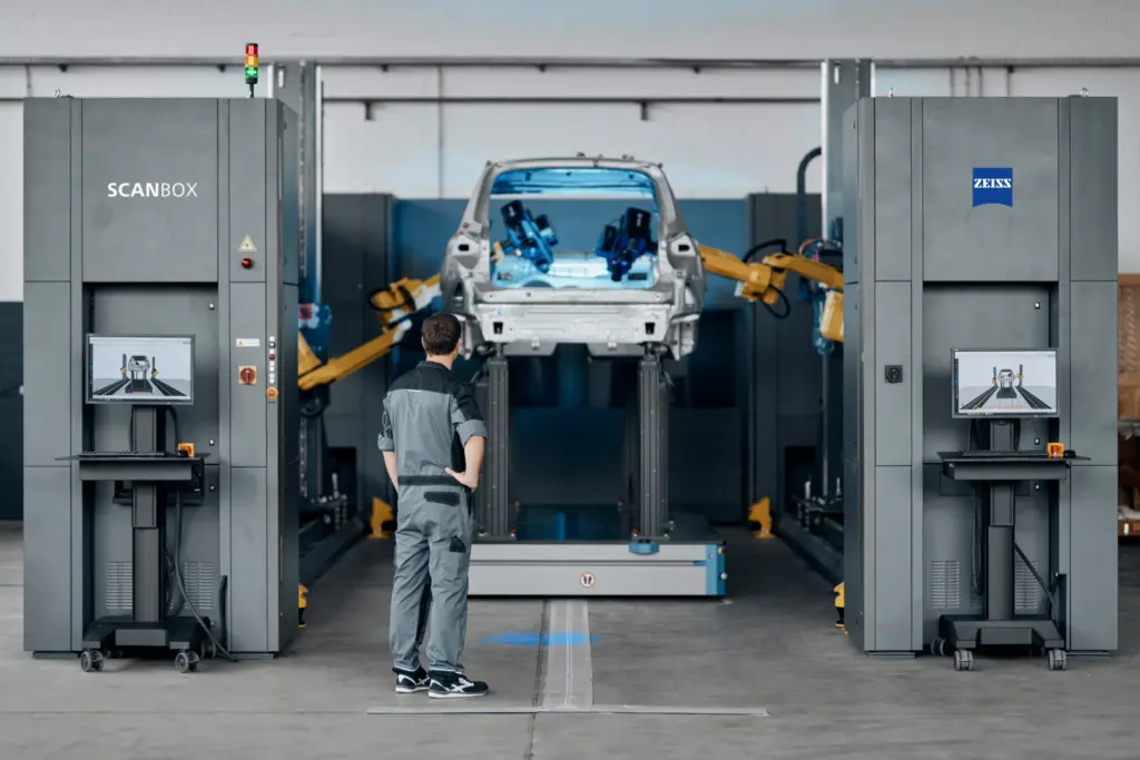 Car body-in-white on a transport shuttle between two ZEISS ScanBox measuring towers, an operator at the control station