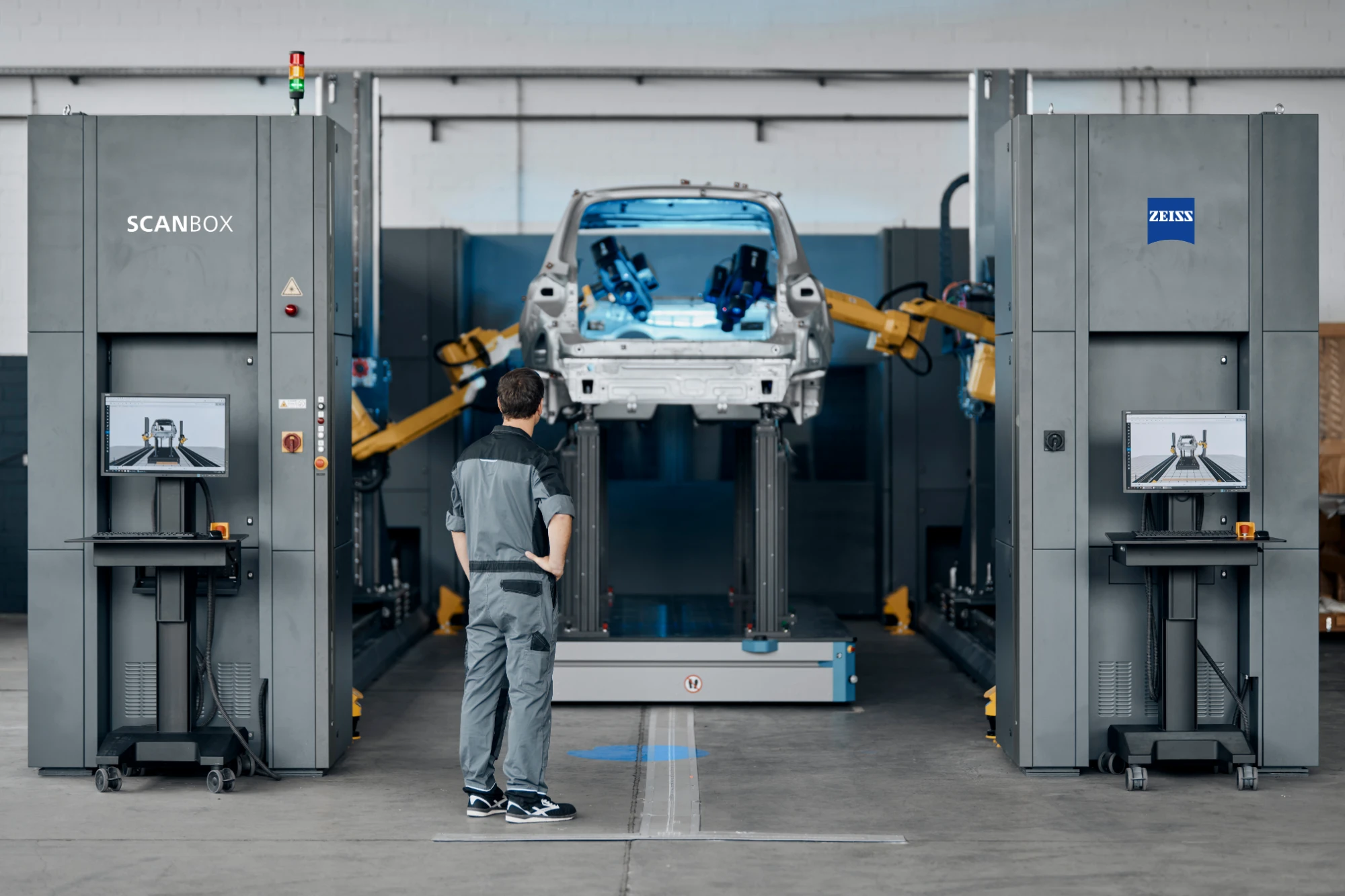 Car body-in-white on a transport shuttle between two ZEISS ScanBox measuring towers, an operator at the control station