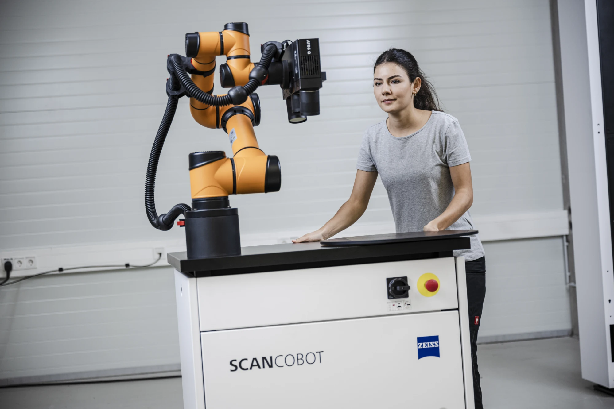 ZEISS ScanCobot: an orange collaborative robot arm carrying a scanner on a wheeled cart, an operator standing alongside