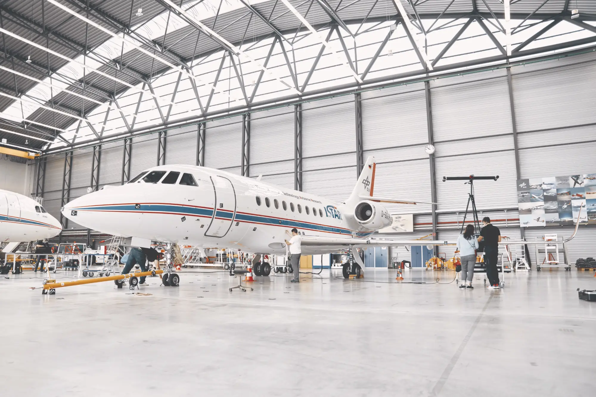 Business jet in a hangar with technicians and a measuring column set up alongside it