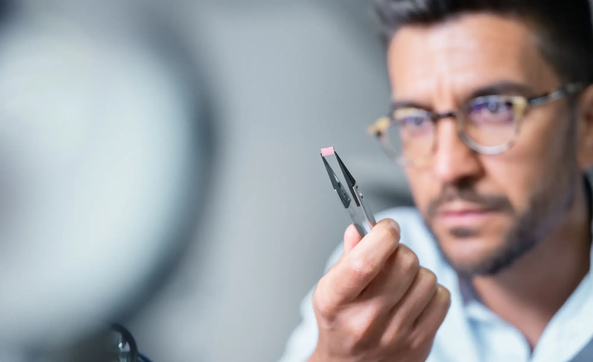 Technician inspecting a millimetre-sized component held in tweezers